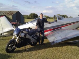 Man standing between a motorcycle and a small airplane outdoors.