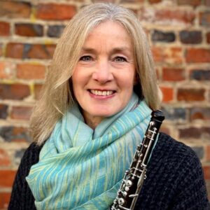 A smiling woman with gray hair, wearing a scarf, holding a clarinet.