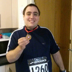 Man holding a medal while wearing a race bib and sports attire.