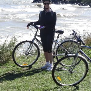 A cyclist standing next to a bicycle by a river on a sunny day.