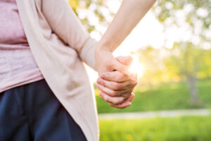 Two people holding hands while walking outdoors on a sunny day.